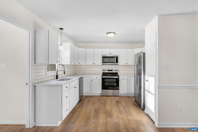 kitchen featuring sink, white cabinetry, pendant lighting, stainless steel appliances, and backsplash