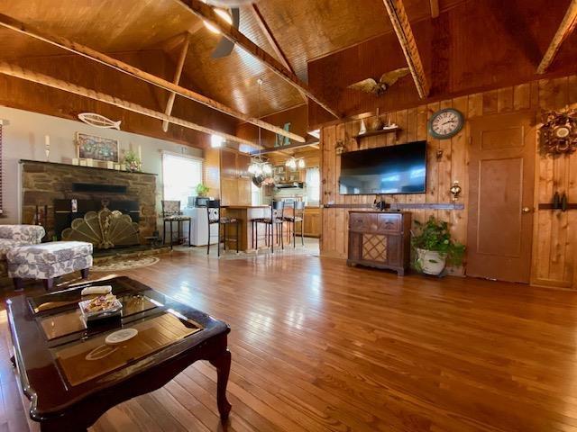living area with wood ceiling, wood finished floors, wood walls, a stone fireplace, and beamed ceiling