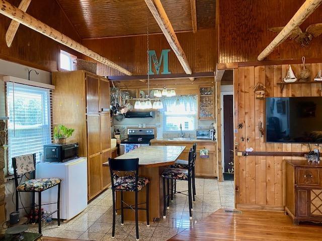 kitchen featuring a kitchen bar, refrigerator, high vaulted ceiling, electric range, and wood walls