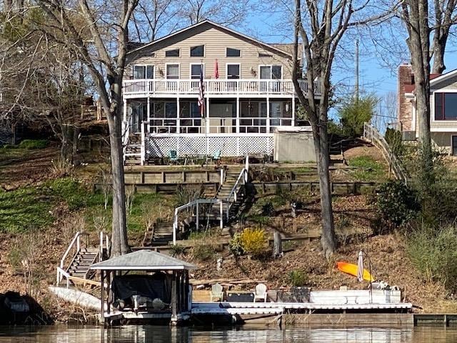 rear view of property with stairway, a sunroom, and a water view