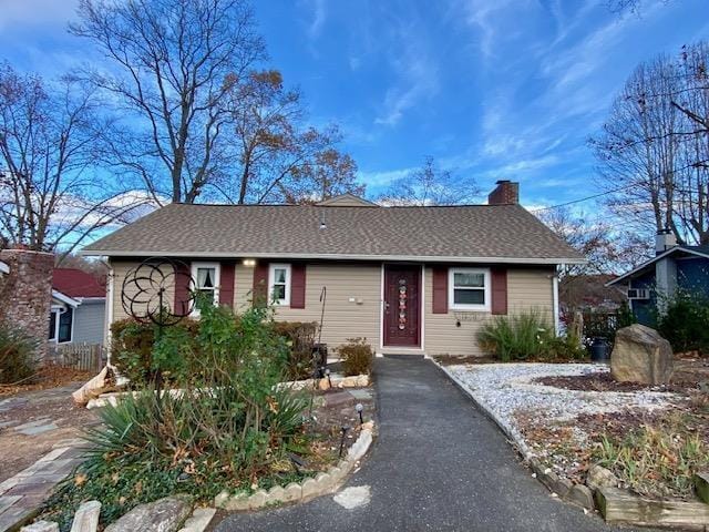 single story home with aphalt driveway, a shingled roof, and a chimney