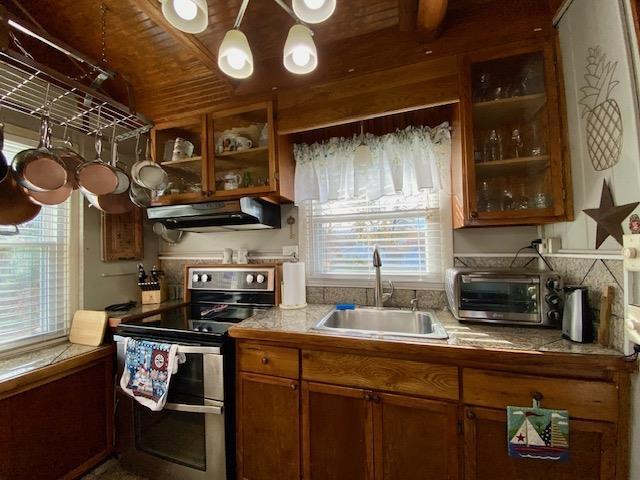 kitchen with a toaster, under cabinet range hood, brown cabinetry, double oven range, and a sink
