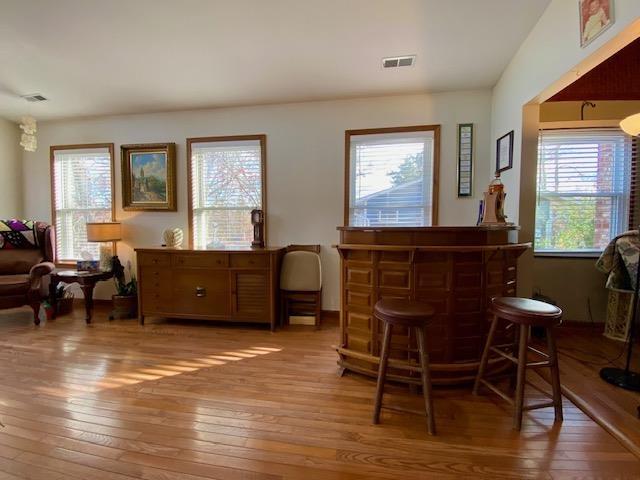 living area with hardwood / wood-style floors, a bar, and visible vents