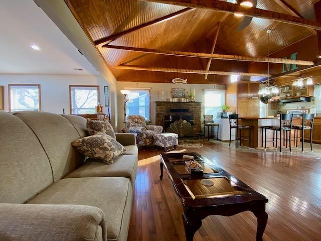 living room featuring high vaulted ceiling, beam ceiling, a fireplace, wooden ceiling, and hardwood / wood-style flooring