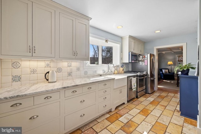 kitchen with stainless steel appliances, backsplash, a sink, light stone countertops, and recessed lighting