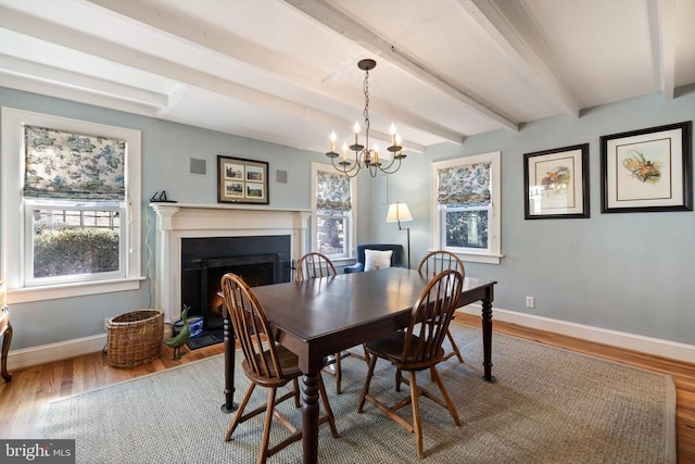 dining room with baseboards, beam ceiling, wood finished floors, a fireplace with flush hearth, and a chandelier
