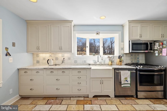 kitchen with appliances with stainless steel finishes, tasteful backsplash, stone tile floors, and light stone counters