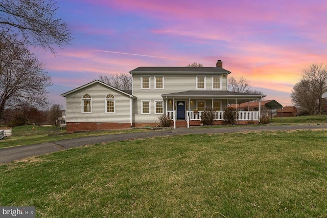 view of front of property with a chimney, covered porch, driveway, and a lawn