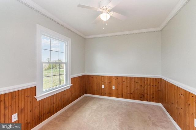 carpeted spare room with wood walls, wainscoting, ceiling fan, and crown molding