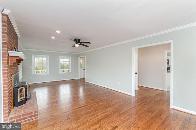 unfurnished living room with light wood-style floors, baseboards, ornamental molding, ceiling fan, and a wood stove