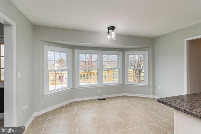 unfurnished dining area with plenty of natural light, light tile patterned floors, and baseboards