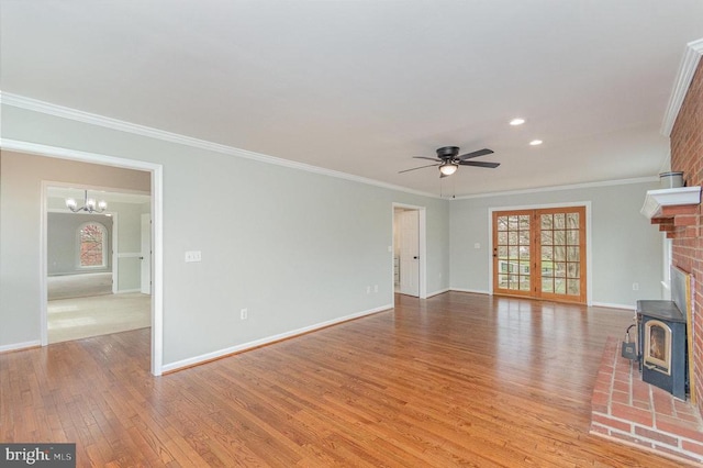 unfurnished living room with crown molding, ceiling fan, a wood stove, wood finished floors, and baseboards