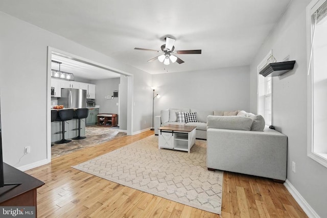 living area featuring ceiling fan, baseboards, and light wood-type flooring