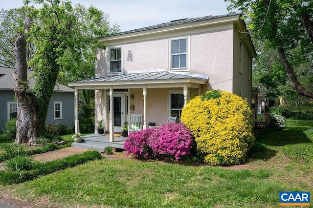 traditional-style home with a porch, stucco siding, metal roof, a front lawn, and a standing seam roof