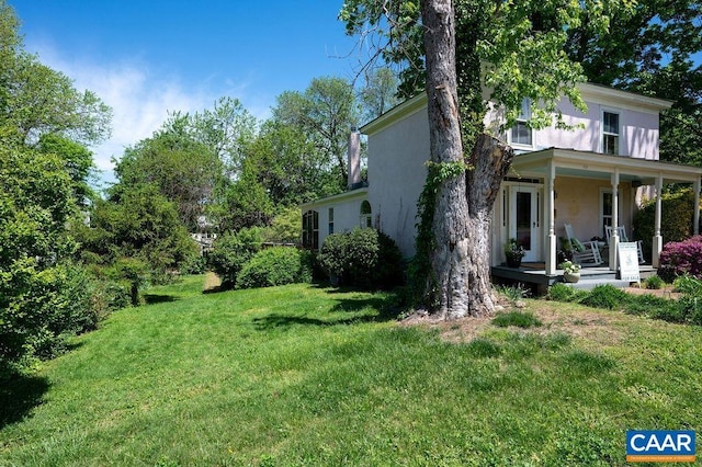 view of property exterior with stucco siding, covered porch, and a yard