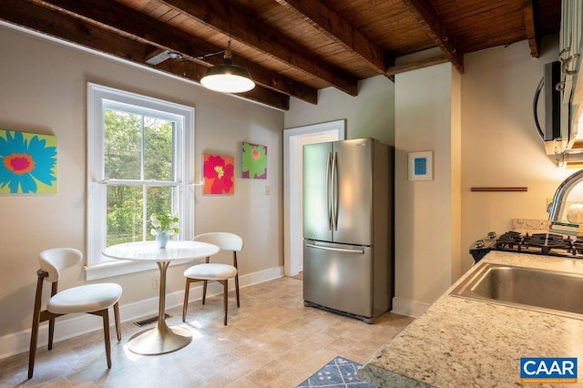 kitchen featuring appliances with stainless steel finishes, wooden ceiling, beam ceiling, light countertops, and light stone finish flooring
