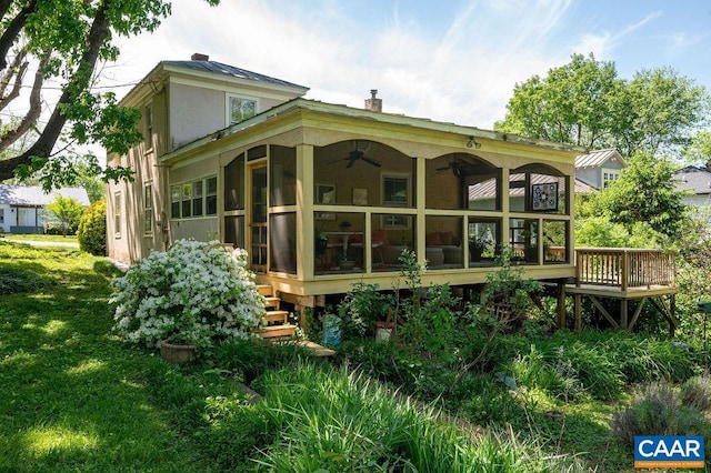 rear view of house with ceiling fan, a sunroom, stucco siding, metal roof, and a lawn