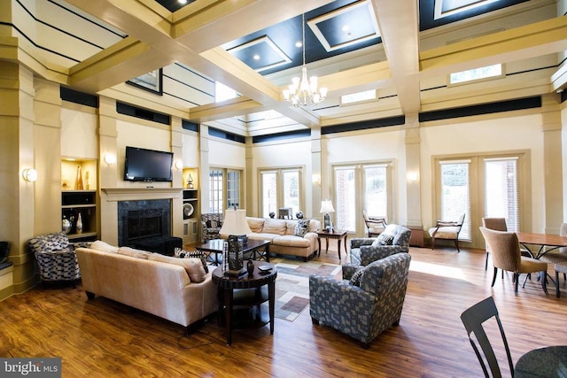 living area with a fireplace, coffered ceiling, wood finished floors, a chandelier, and beamed ceiling