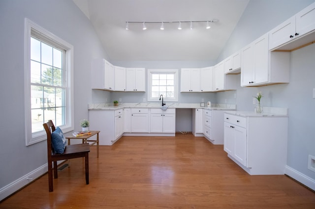 kitchen with a sink, lofted ceiling, light wood-type flooring, track lighting, and baseboards