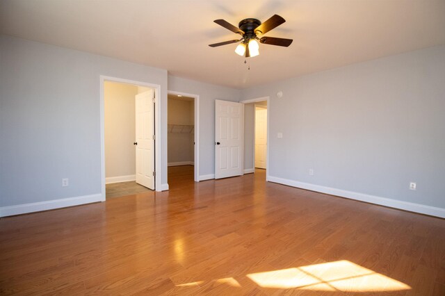 unfurnished bedroom featuring a ceiling fan, a closet, baseboards, a walk in closet, and light wood-style floors