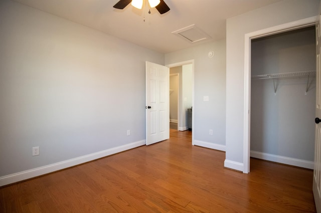 unfurnished bedroom featuring a closet, wood finished floors, attic access, a ceiling fan, and baseboards