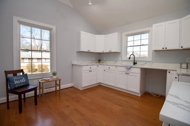kitchen featuring light wood-style flooring, a baseboard radiator, white cabinets, light stone counters, and lofted ceiling