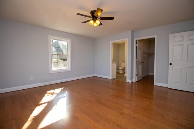 unfurnished bedroom with baseboards, a spacious closet, and wood finished floors