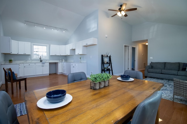 dining space featuring rail lighting, high vaulted ceiling, a ceiling fan, and dark wood-style floors