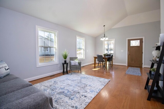 living room featuring an inviting chandelier, wood finished floors, visible vents, baseboards, and lofted ceiling