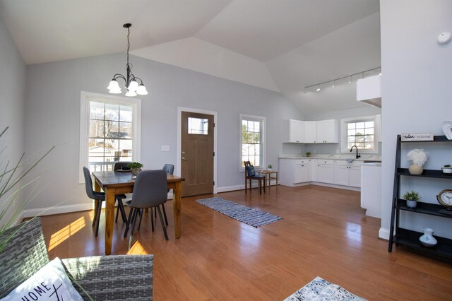 dining area with an inviting chandelier, light wood-style flooring, rail lighting, baseboards, and lofted ceiling