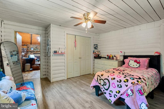 bedroom with light wood-style floors, a closet, wooden ceiling, ceiling fan, and wood walls