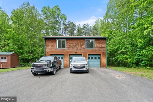 rustic home with asphalt driveway, an attached garage, a storage shed, and an outbuilding