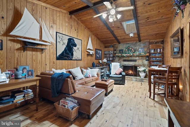 living area featuring wood ceiling, wood walls, hardwood / wood-style floors, a stone fireplace, and a ceiling fan