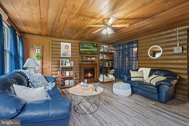 living room featuring rustic walls, wood finished floors, wooden ceiling, a lit fireplace, and ceiling fan