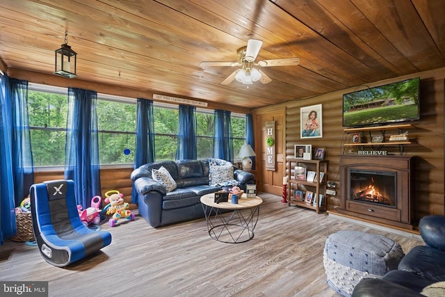 living area with wooden ceiling, wood finished floors, a warm lit fireplace, rustic walls, and ceiling fan