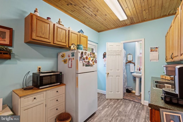 kitchen featuring black microwave, freestanding refrigerator, light wood-type flooring, crown molding, and wooden ceiling