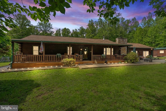 back of house at dusk with log siding, a chimney, a lawn, and a porch