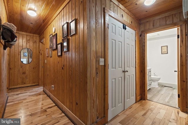 hallway featuring wooden ceiling, light wood-type flooring, wood walls, and baseboards