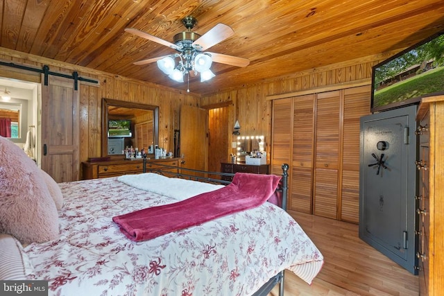 bedroom with a barn door, wood ceiling, wood walls, a closet, and light wood-style flooring