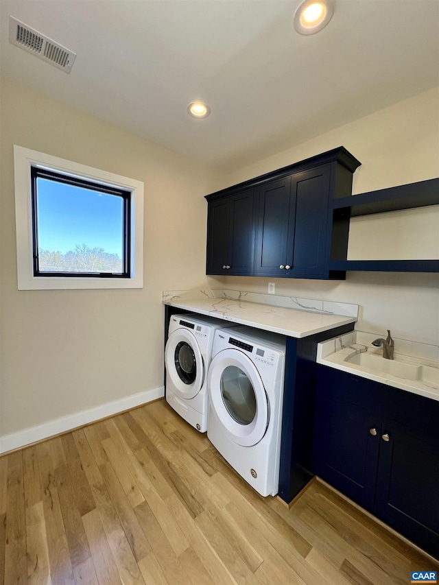 laundry area with washer and clothes dryer, a sink, cabinet space, visible vents, and light wood-style floors
