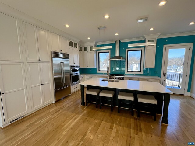 kitchen featuring light wood-style flooring, wall chimney exhaust hood, stainless steel appliances, crown molding, and light countertops