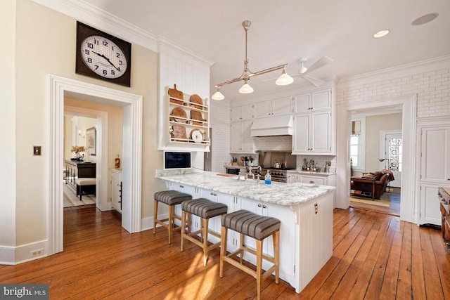 kitchen featuring a peninsula, ornamental molding, white cabinetry, and wood-type flooring