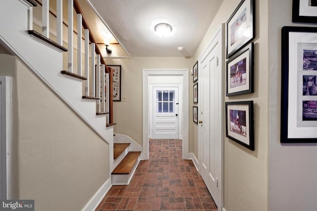 doorway with brick patterned floor, baseboards, and stairway