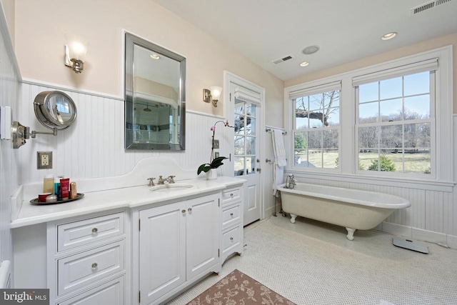 bathroom with vanity, a freestanding tub, wainscoting, and visible vents