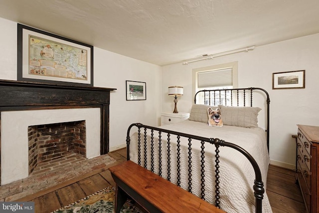 bedroom featuring baseboards, a fireplace with raised hearth, and hardwood / wood-style flooring