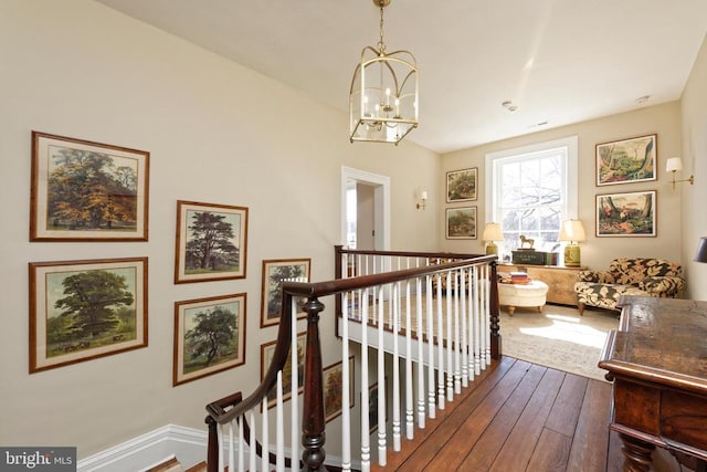 hallway with an upstairs landing, an inviting chandelier, and dark wood-style floors