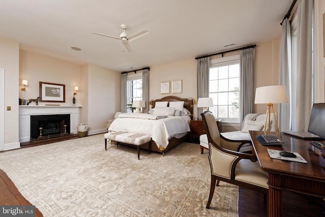 bedroom featuring multiple windows, wood finished floors, baseboards, and a fireplace with raised hearth