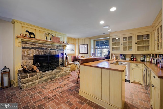 kitchen with brick floor, dishwasher, cream cabinets, and butcher block countertops