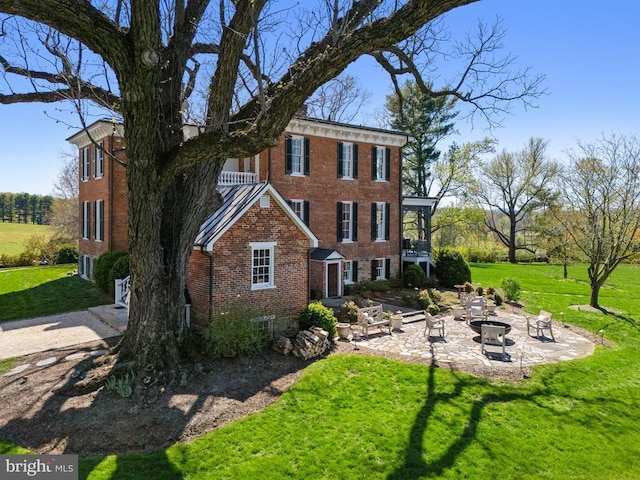 rear view of property with an outdoor fire pit, brick siding, a lawn, and a patio area