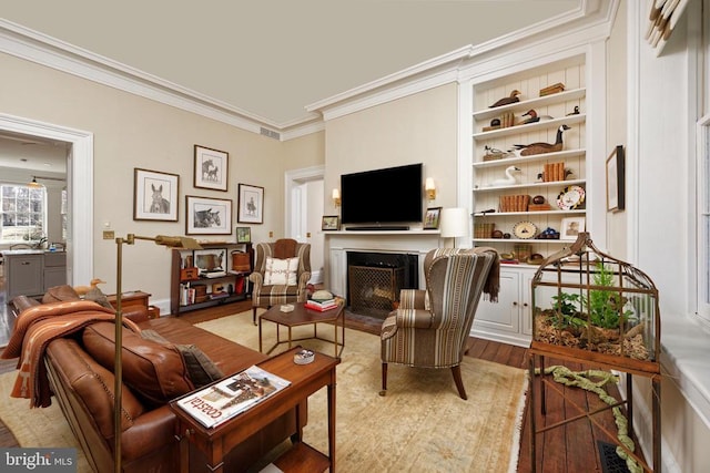 living room featuring wood finished floors, a fireplace, visible vents, baseboards, and ornamental molding